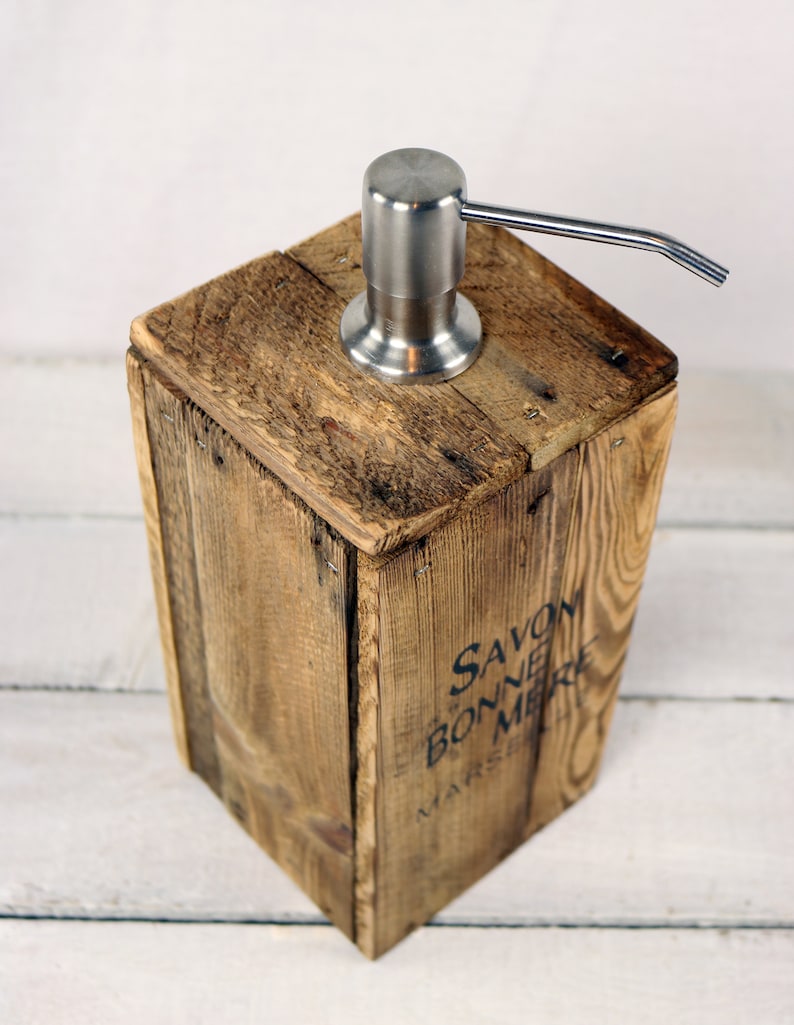 May include: A wooden soap dispenser with a stainless steel pump. The dispenser is made from reclaimed wood and has the words "Savon de Bonne Mere Marseille" printed on the side.