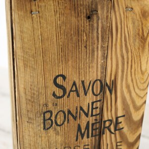 May include: A wooden box with the text "Savon la Bonne Mere Marseille" printed on the front. The box is made of natural wood with a rustic finish.
