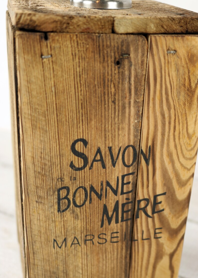 May include: A wooden box with the text "Savon la Bonne Mere Marseille" printed on the front. The box is made of natural wood with a rustic finish.