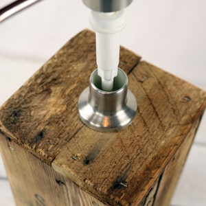 May include: A stainless steel soap dispenser pump being inserted into a wooden soap dispenser. The dispenser is made from reclaimed wood and has a rustic look.