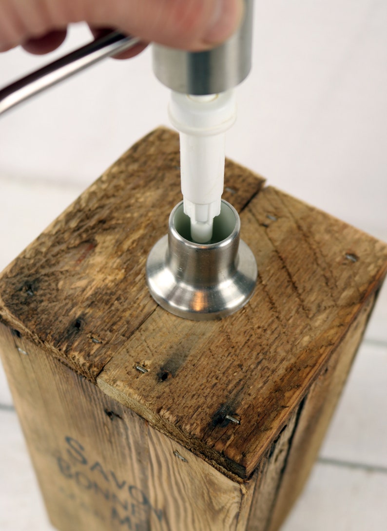 May include: A stainless steel soap dispenser pump being inserted into a wooden soap dispenser. The dispenser is made from reclaimed wood and has a rustic look.