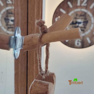 Puede incluir: Una rama de madera con una cuerda atada a ella. La rama está unida a una ventosa en un espejo. La rama cuelga de la cuerda y tiene un bloque de madera al final de la cuerda. El texto "Timbert" es visible en la esquina inferior derecha de la imagen.