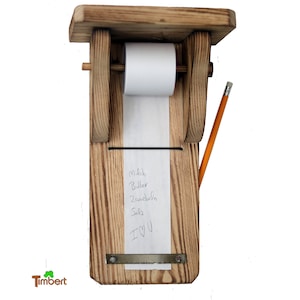 以下が含まれることがあります： 木製のメモ帳ホルダーに、紙のロールと鉛筆が置かれています。紙には、「Milk, Butter, 2 Zwiebeln, Salz, I ♥ U」という手書きの買い物リストが書かれています。