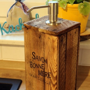 May include: A wooden soap dispenser with a stainless steel pump. The dispenser is labeled "Savon Bonne Mere Marseille".