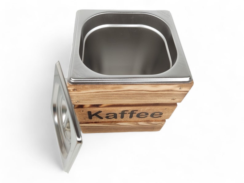 May include: A wooden box with a stainless steel container inside. The box has the word "Kaffee" printed on the front. The container has a lid that is open and sitting next to the box.
