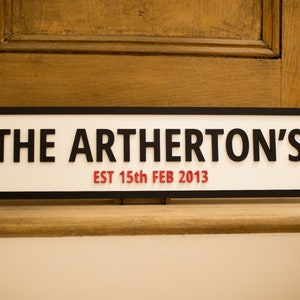 May include: A white sign with black trim and black lettering that reads "THE ARTHERTON'S EST 15th FEB 2013".