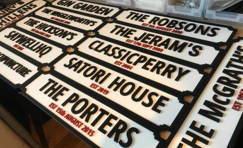 May include: A collection of white and black street signs with the names of businesses and their establishment dates. The signs are made of wood and have a vintage look.