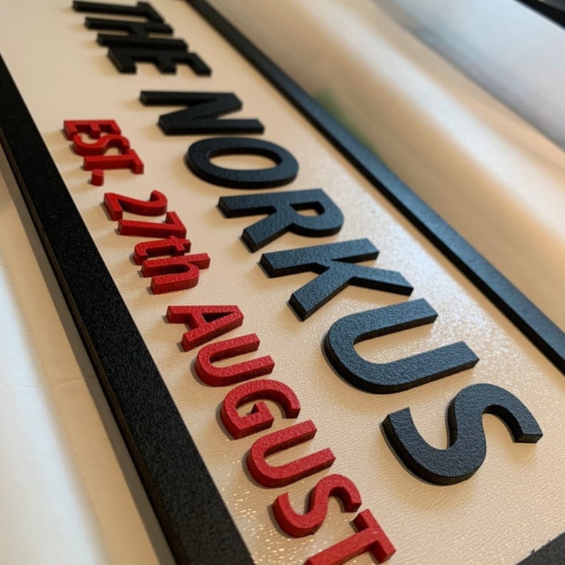 May include: A black and white sign with the text "The Norkus Est. 27th August" in raised letters. The text "The Norkus" is in black and the text "Est. 27th August" is in red.