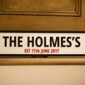 May include: A white sign with black trim and the text "THE HOLMES'S EST 17th JUNE 2017" in black and red lettering.
