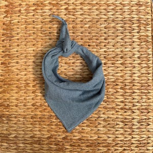 May include: A triangular pet bandana made of a grey fabric with a fine white pinstripe pattern. The fabric is tied at the top into a knot, creating a circular opening for the neck, with the pointed end of the bandana hanging downward.