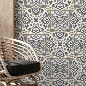 May include: A white wicker chair with a black cushion sits in front of a wall covered in patterned wallpaper. The wallpaper features a repeating design of grey and gold floral motifs.