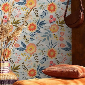 May include: A room scene featuring a floral wallpaper with orange, yellow, and blue flowers. A brown leather purse hangs on a wooden panel. An orange ottoman with a corduroy pillow and a vase with dried plants complete the decor.