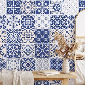 Könnte beinhalten: Ein Schlafzimmer mit einer Wand, die mit blau-weiß gemusterten Fliesen verziert ist. Eine Holzbank trägt eine Vase mit Trockenblumen, Büchern und einer Decke. Ein großer Spiegel und ein Bett sind im Hintergrund zu sehen, was eine gemütliche Atmosphäre schafft.