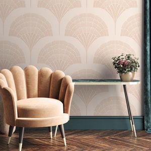 May include: A beige armchair with a scalloped back sits in front of a wall with a pink and white geometric pattern wallpaper. A small table with a dark green top and gold legs sits next to the chair. A potted plant with green leaves and pink flowers sits on the table.