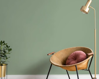 May include: A mid-century modern interior scene featuring a tan leather chair with a pink round pillow. A gold floor lamp and a potted plant in a gold planter are also present. The background is a muted green wall, and the floor is wood.