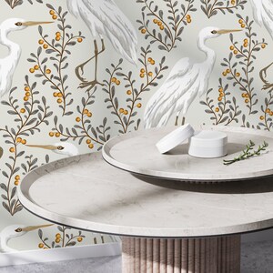 May include: White ceramic table with two round tiers. The table has a light wood base. The background is a white wallpaper with a repeating pattern of white birds and gray branches with orange berries.