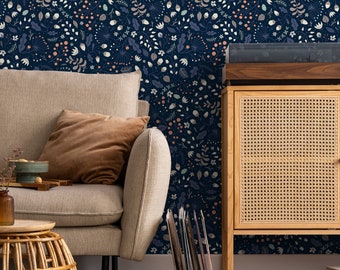 May include: A beige sofa with a brown throw pillow sits in front of a wall with a dark blue floral wallpaper. A wooden cabinet with a woven rattan door is to the right of the sofa. A stack of vinyl records is leaning against the cabinet.