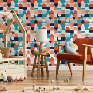 May include: A child's room with a colorful geometric patterned wallpaper in shades of orange, teal, navy, and white. The room features a wooden bed frame, a small wooden table with a lamp, and an orange armchair. A plush snail pillow rests on the chair.