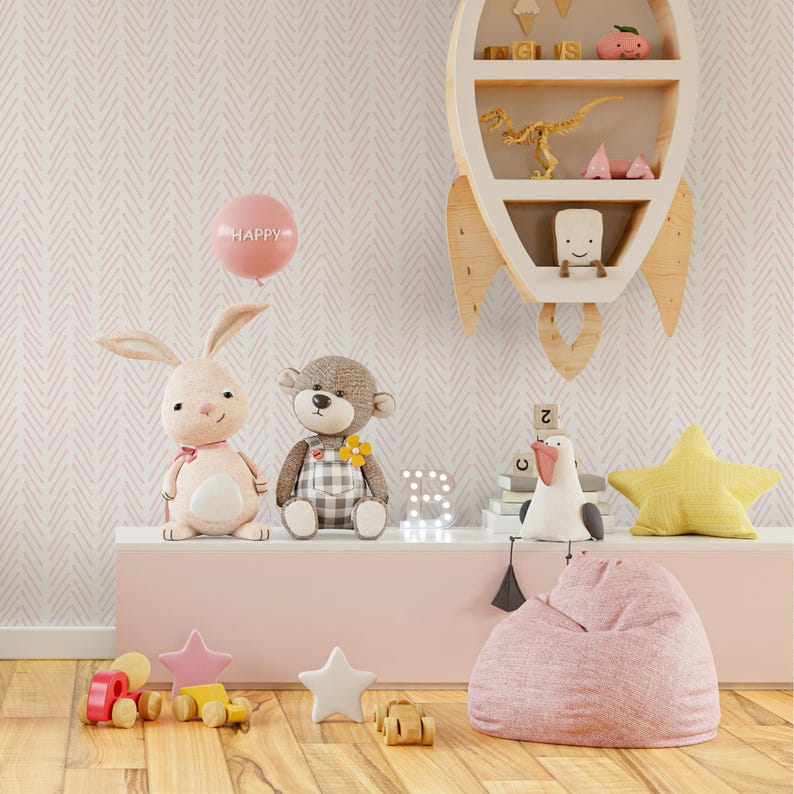 K&ouml;nnte beinhalten: Ein Kinderzimmer mit einem rosa-wei&szlig;en Chevron-Muster, einem rosa Sitzsack, einem Stoffhasen und -b&auml;ren, einem h&ouml;lzernen Raketenregal mit Spielzeug und einem rosa Ballon mit der Aufschrift "Happy".