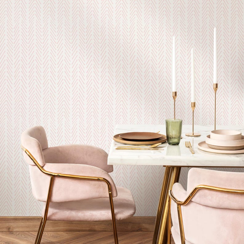 K&ouml;nnte beinhalten: Ein wei&szlig;er Esszimmer mit rosa Chevron-Tapete. Zwei rosa St&uuml;hle mit goldenen Rahmen stehen an einem wei&szlig;en Marmortisch mit goldenen Beinen. Auf dem Tisch stehen drei goldene Kerzenhalter mit wei&szlig;en Kerzen und ein Glas Wasser.