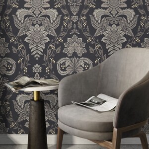 May include: A gray armchair with a magazine on the seat sits in front of a dark gray wall with a white and gold damask pattern. A small round table with a white top and a black base sits next to the chair.