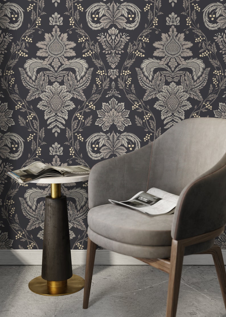 May include: A gray armchair with a magazine on the seat sits in front of a dark gray wall with a white and gold damask pattern. A small round table with a white top and a black base sits next to the chair.
