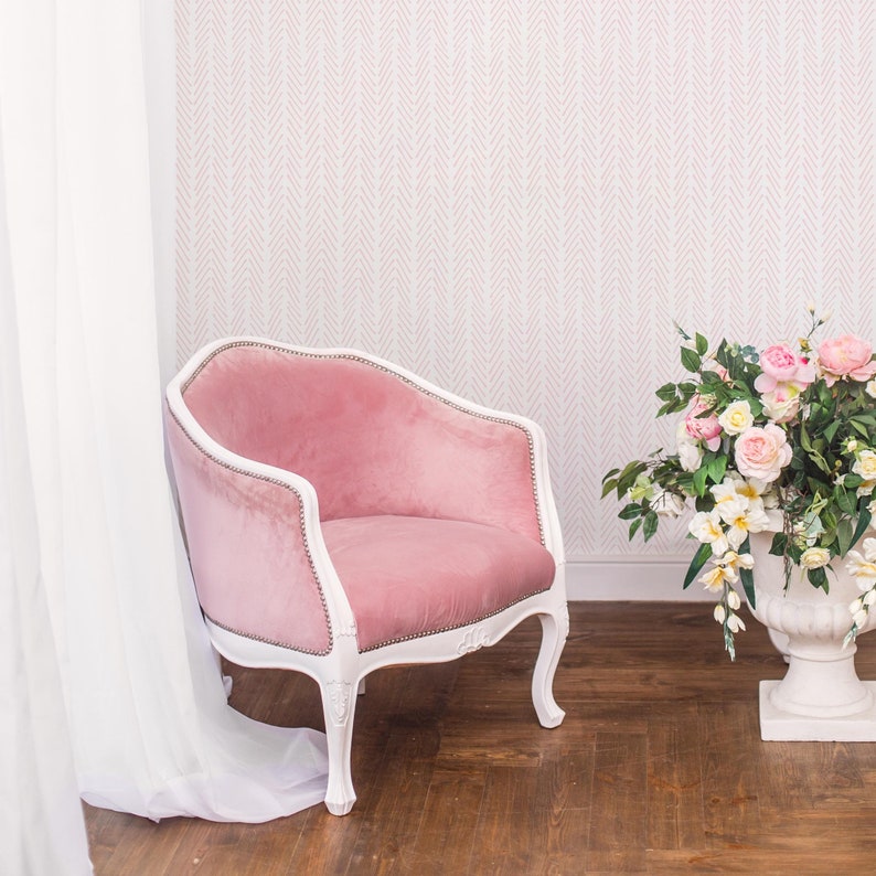 K&ouml;nnte beinhalten: Ein rosa Samt-Sessel mit wei&szlig; lackierten Beinen und einem wei&szlig;en Hintergrund. Der Sessel steht in einem Raum mit einem wei&szlig;en Vorhang und einem Strau&szlig; rosa und wei&szlig;er Blumen in einer wei&szlig;en Vase.