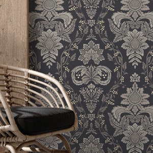 May include: A wicker chair with a black cushion sits in front of a wall with a dark blue and cream floral wallpaper pattern.