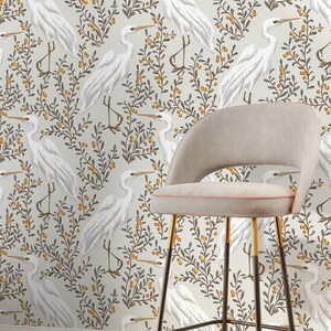 May include: White egret birds on a beige background with grey and yellow foliage. The birds are repeated in a pattern. A bar stool with a beige seat and black and gold metal legs is in the foreground.