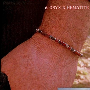 Peut inclure: Un bracelet en perles avec des pierres précieuses rouges, noires et bleues. Le bracelet est composé d'un mélange de perles rondes et rectangulaires. Le bracelet est présenté sur le poignet d'une personne.