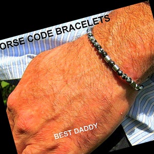 Könnte beinhalten: Ein schwarz-weißes Perlenarmband mit silbernen Akzenten. Das Armband wird am Handgelenk einer Person getragen und der Text "BEST DADDY" ist am Handgelenk sichtbar. Das Armband ist mit "MORSE CODE BRACELETS" beschriftet.