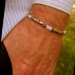May include: A silver and gold bracelet with a light blue opal and hematite beads. The bracelet is on a person's wrist.