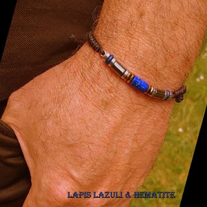 以下が含まれることがあります： 濃いコードと、青いラピスラズリと銀色の金属ビーズを特徴とする中央のデザインのブレスレット。ブレスレットには、金色のビーズと濃い青色のビーズも含まれています。「LAPIS LAZULI & HEMATITE」というテキストが表示されています。