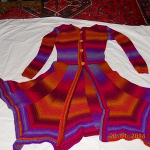 May include: A vibrant, handmade crochet cardigan in a spectrum of colours, including red, orange, and purple. It features long sleeves, a flared skirt, and wooden buttons. The garment is displayed on a white surface.