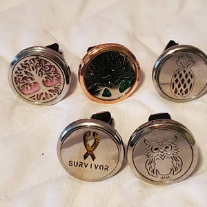 May include: Six silver car air fresheners with different designs. The designs include a tree of life, a pineapple, an owl, a ribbon with the word "SURVIVOR", and two different tree designs.