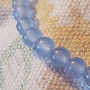 May include: A light blue beaded bracelet with a frosted finish. The beads are round and smooth.