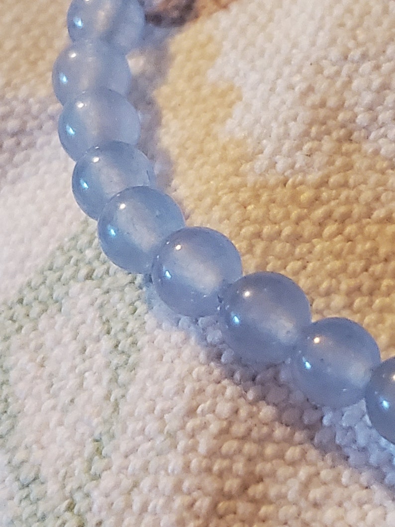 May include: A light blue beaded bracelet with a frosted finish. The beads are round and smooth.