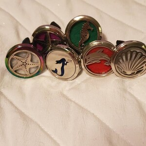 May include: Six silver car air fresheners with different sea-themed designs. The designs include a starfish, a mermaid, a dolphin, a seashell, a seahorse, and a starfish with a purple background.