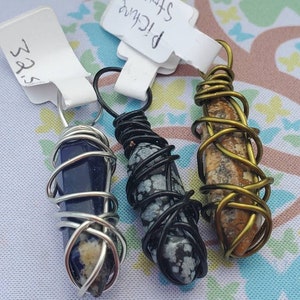 May include: Three wire-wrapped crystal pendants. The pendants are made with silver, black, and gold wire. The crystals are blue, black and white speckled, and brown and white speckled.