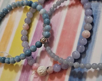 May include: Three beaded bracelets in shades of blue and lavender. One bracelet has a white lava bead charm.