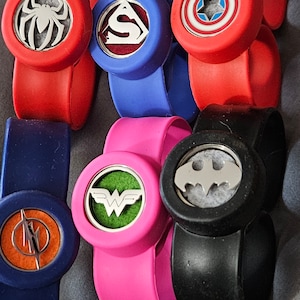 May include: Six colorful silicone bracelets with different superhero logos. Each bracelet has a round, removable, silver-colored disc with a different superhero logo. The logos include Spiderman, Superman, Captain America, Wonder Woman, Batman, and The Flash.