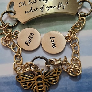 May include: Gold chain bracelet with a charm that reads "What if I fall? Oh, but my Darling... what if you fly?" and two charms that read "Faith" and "Love". The bracelet also has a bee charm.