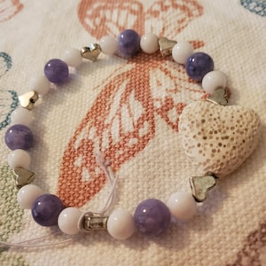 May include: A purple and white beaded bracelet with silver heart charms and a large white heart charm.