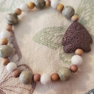 May include: A bracelet made of brown, white, and green beads with a purple lava rock charm.