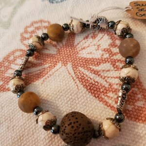 May include: A brown and white beaded bracelet with a brown wood bead and silver accents.