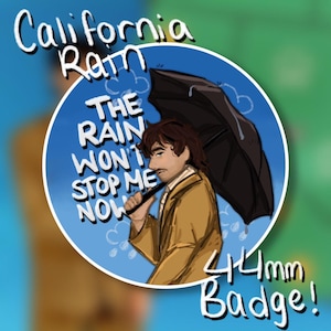 May include: A round badge with a blue background featuring a man holding a black umbrella. The text "California Rain" and "The Rain Won't Stop Me Now" are displayed. The badge is 4.4cm in size.