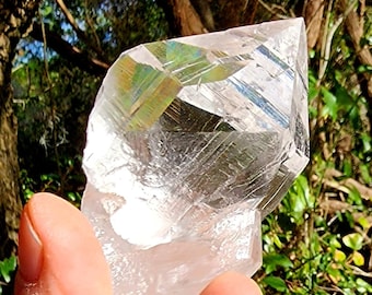 May include: A large, clear quartz crystal with a double termination. The crystal has a rainbow iridescence and is held in a hand.