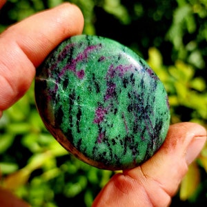 Puede incluir: Una piedra pulida verde y rosa con marcas negras y blancas. La piedra es lisa y de forma ovalada.