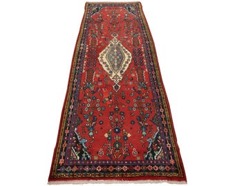 May include: A rectangular red rug with an intricate floral pattern. The rug features a central diamond-shaped medallion in cream, blue, and gold, surrounded by detailed floral and geometric designs. The rug's border is a dark blue with additional floral motifs.