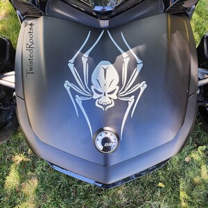 a close-up view of a motorcycle, specifically focusing on the front part of the vehicle. The motorcycle has a distinctive design, including a skull and spider motif, which is prominently displayed on the front grille.